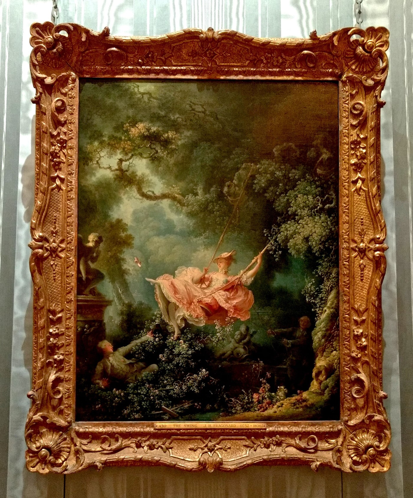 Jean-Honoré Fragonard's The Swing in its ornate gilded frame at the Wallace Collection, with a woman in a luminous pink dress suspended above a dark garden.