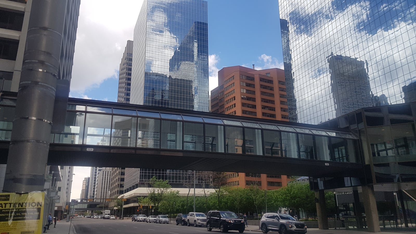 A glass-enclosed +15 pedestrian bridge spans Fifth Avenue SW beneath mirrored office towers in downtown Calgary.