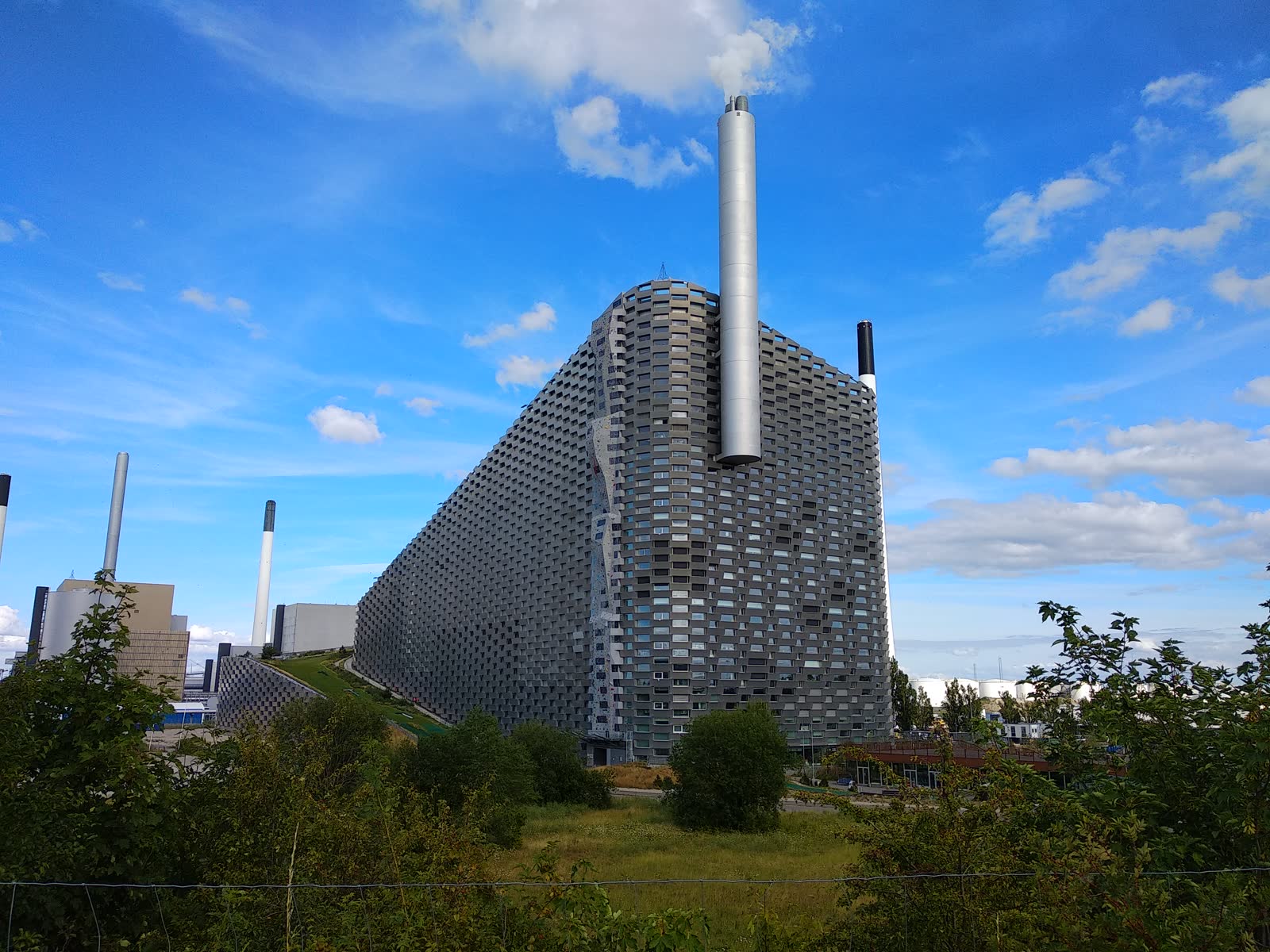 CopenHill and Amager Bakke in Copenhagen, with the sloped building, green roof edge, chimney, and industrial waterfront visible.