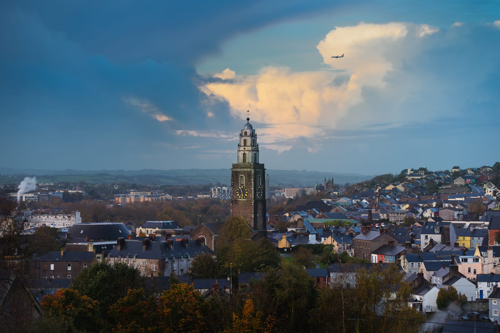 St Anne's Shandon tower and two black-and-gold clock faces rising above Cork's hillside houses beneath a blue-and-gold sky.
