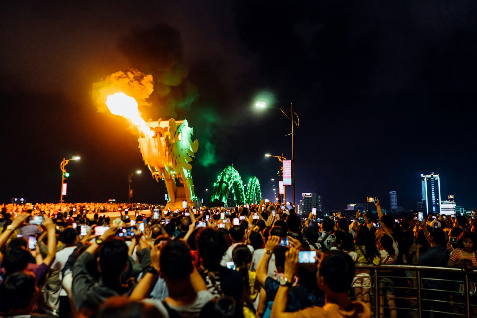 岘港龙桥灯火通明的龙头喷出一团火焰，夜色中密集的人群纷纷举起手机。