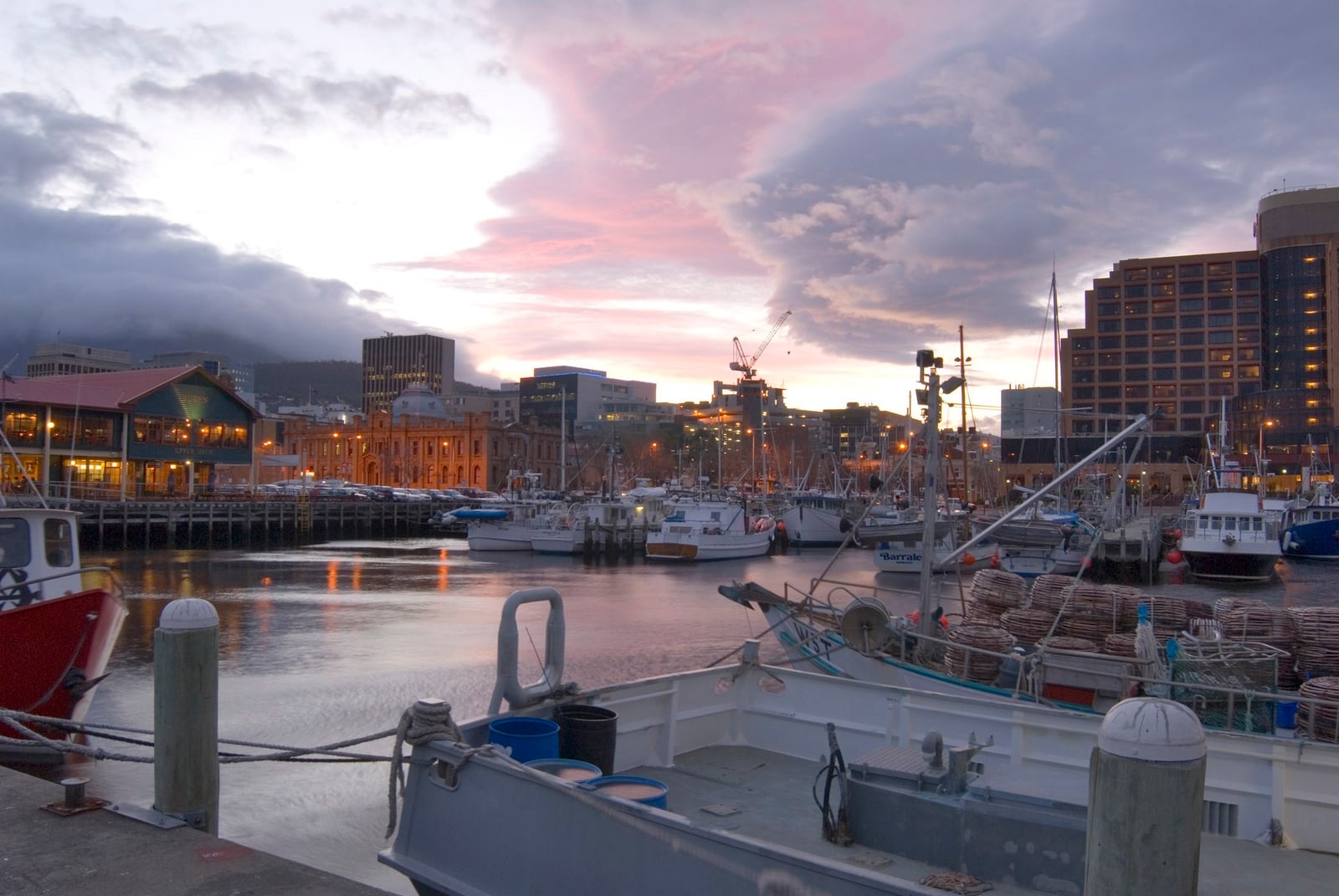 Fishing boats moored in Constitution Dock at dusk, with Hobart's waterfront buildings reflected in calm water.