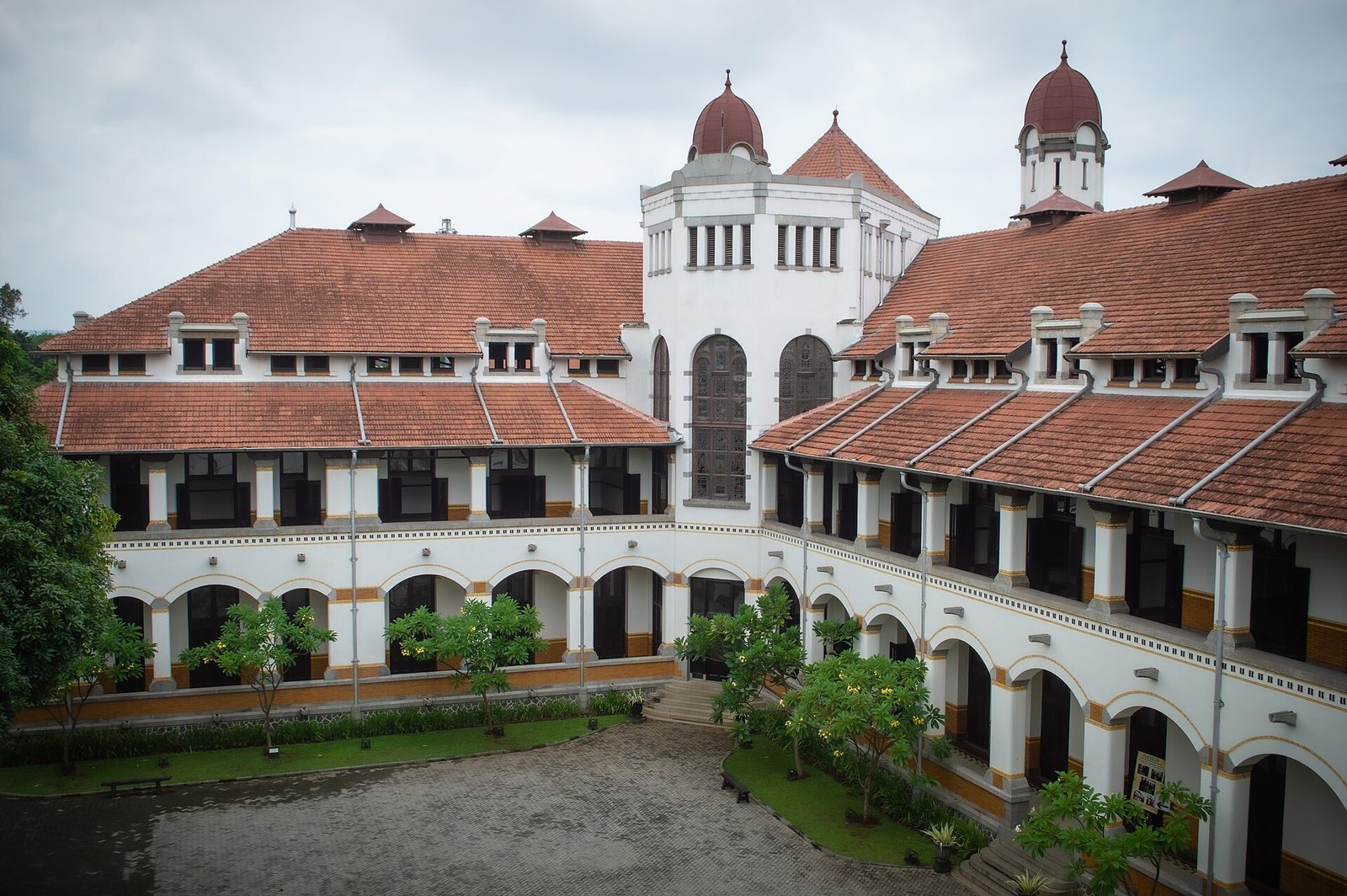 White arcades, dark wooden doors, red-tiled roofs, and vented towers enclose the central courtyard of Lawang Sewu in Semarang.