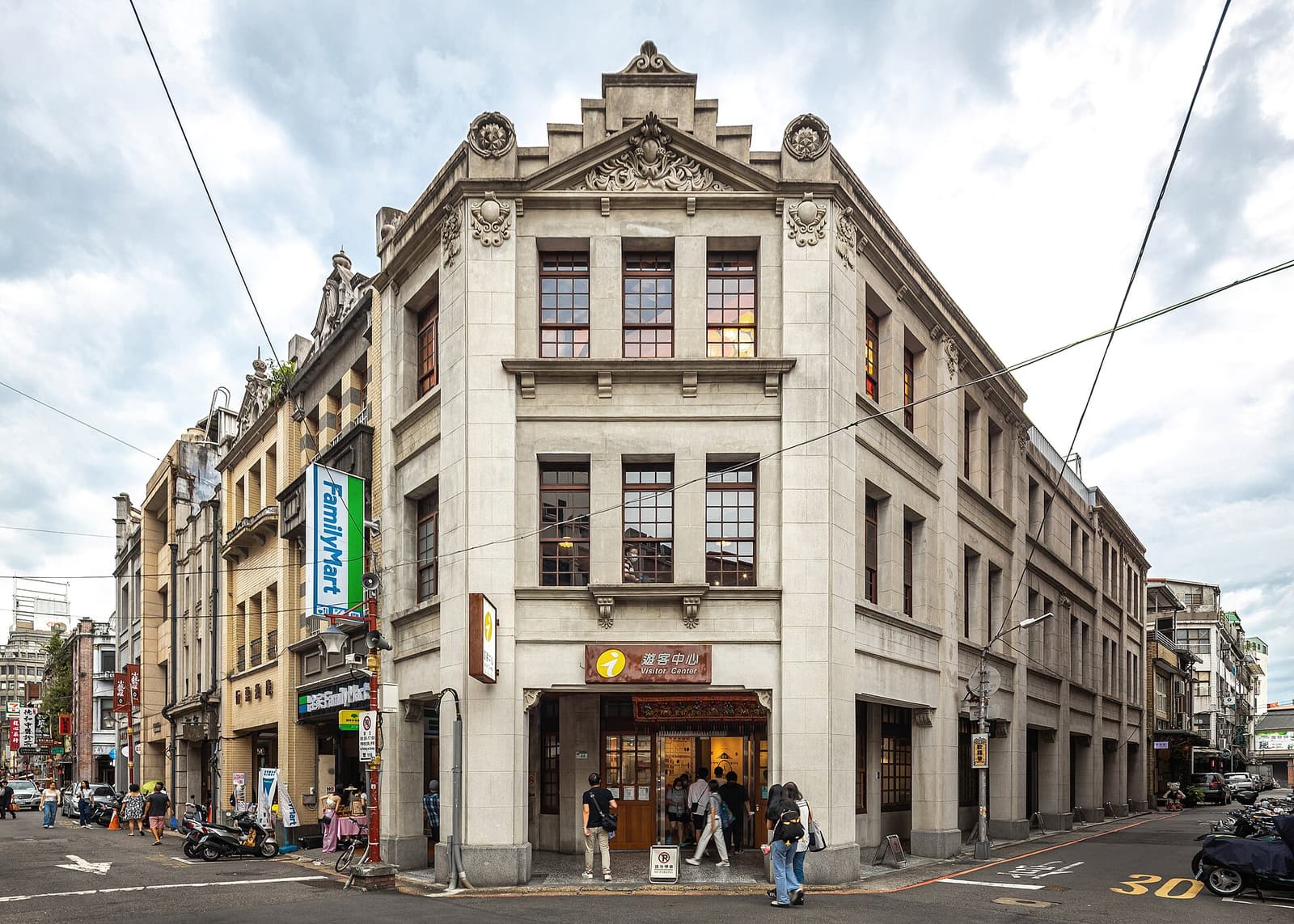 台北迪化街上的大稻埕游客中心，画面中可见历史店屋建筑、街道招牌、行人、机车与沿街店面。
