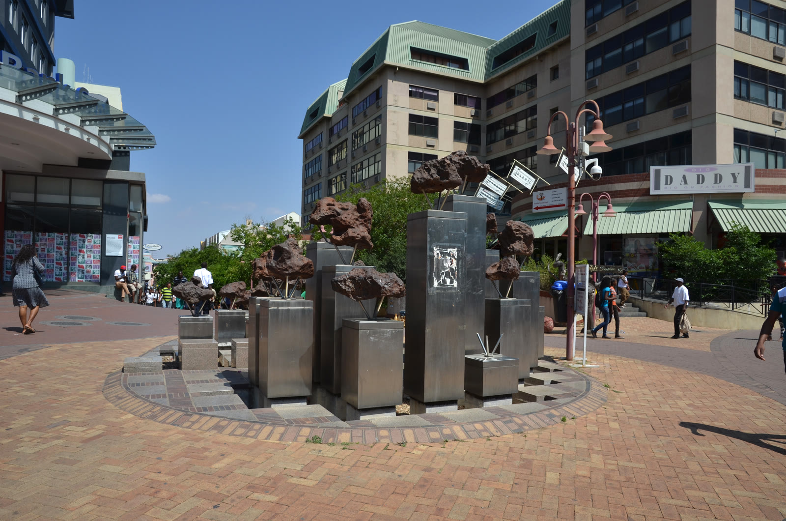 Gibeon iron meteorite fragments mounted on steel plinths among pedestrians and shops in Windhoek's Post Street Mall.