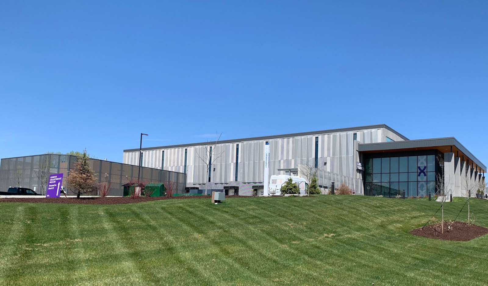蓝天下，威斯康星州麦迪逊的 Exact Sciences 低层现代实验室建筑，玻璃入口旁立有公司标志。