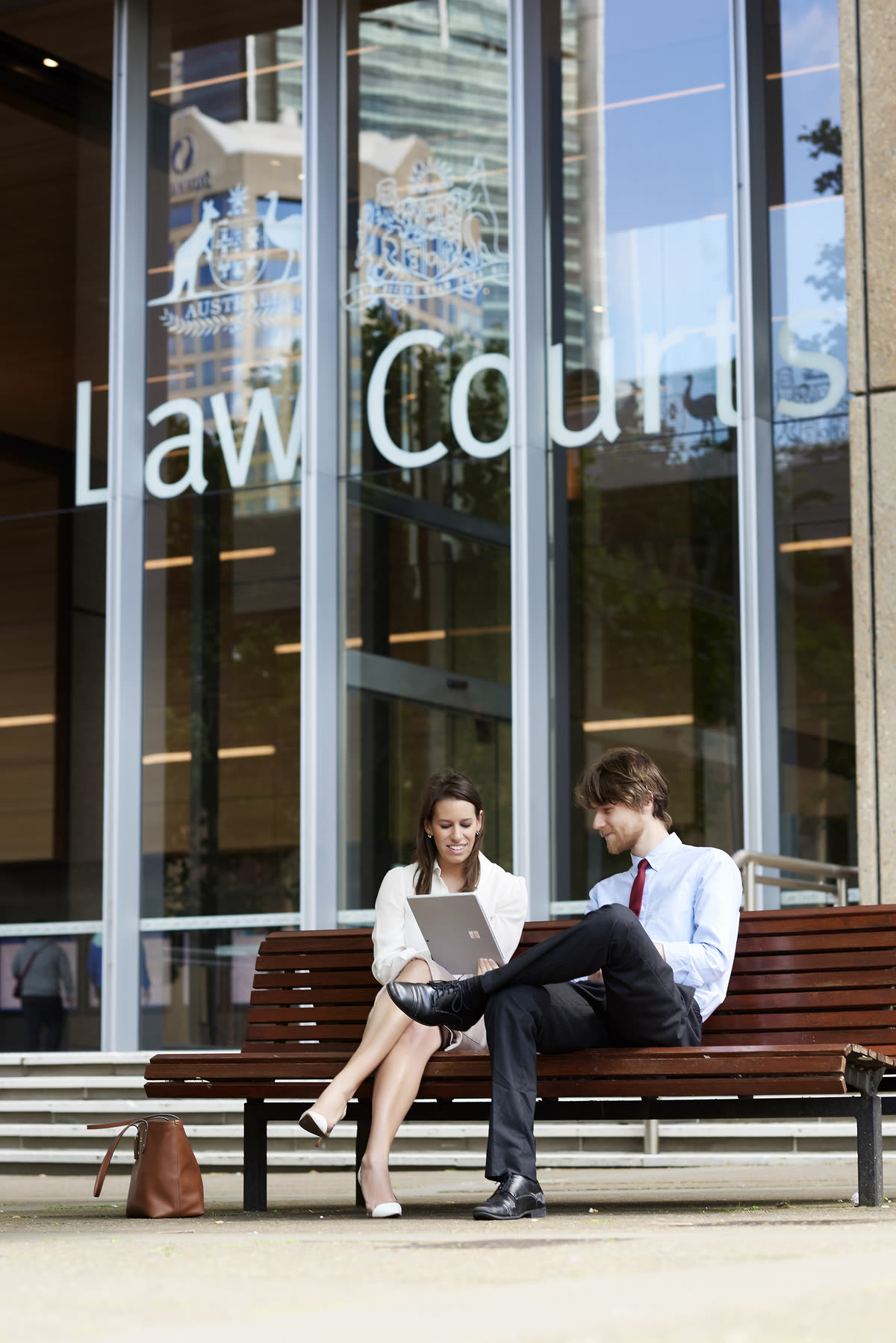 Two lawyers sit outside an Australian law courts building and review work together on a tablet.