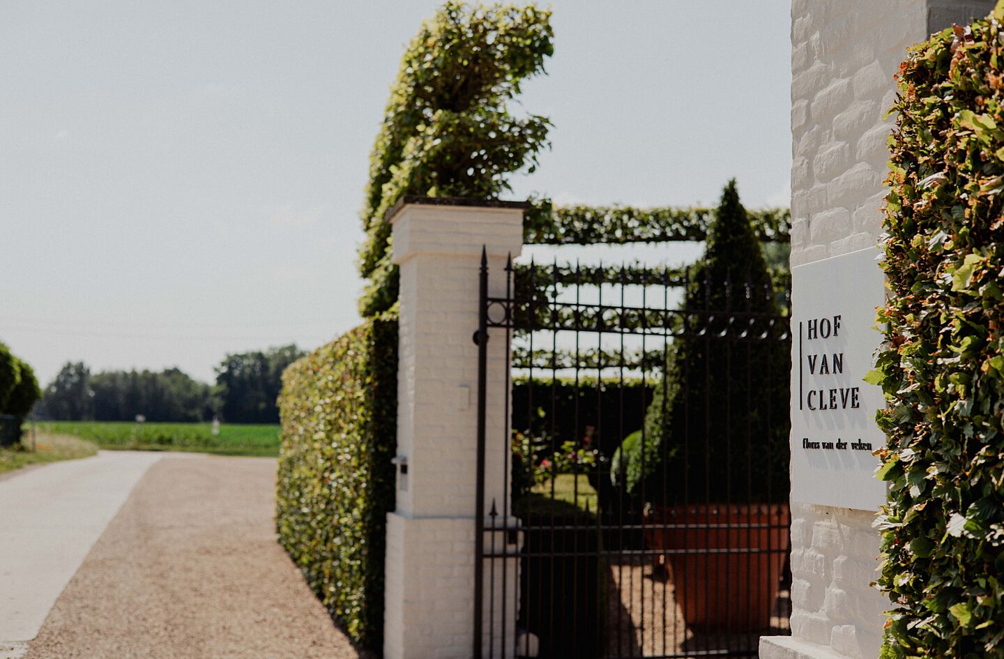 The Hof van Cleve entrance gate and sign in Kruisem, Belgium, photographed beside green fields in summer light.