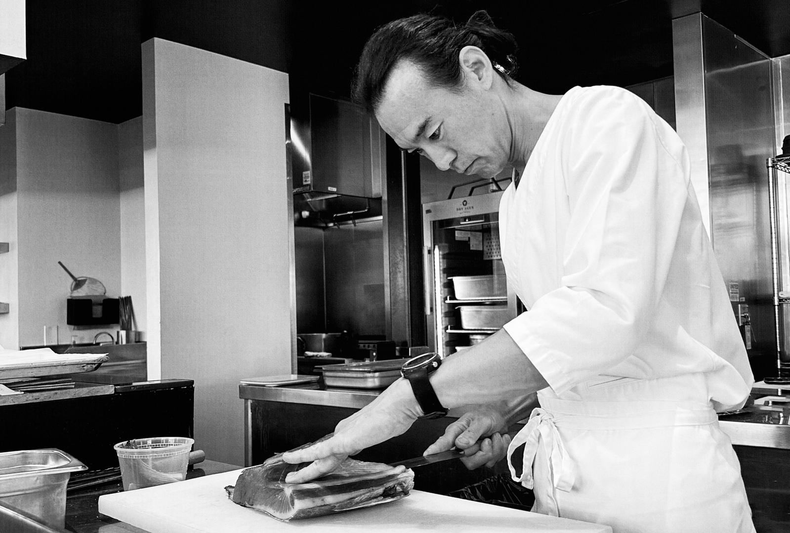 Chef Junya Yamasaki cutting a fish fillet on a board in the kitchen at YESS in Los Angeles.