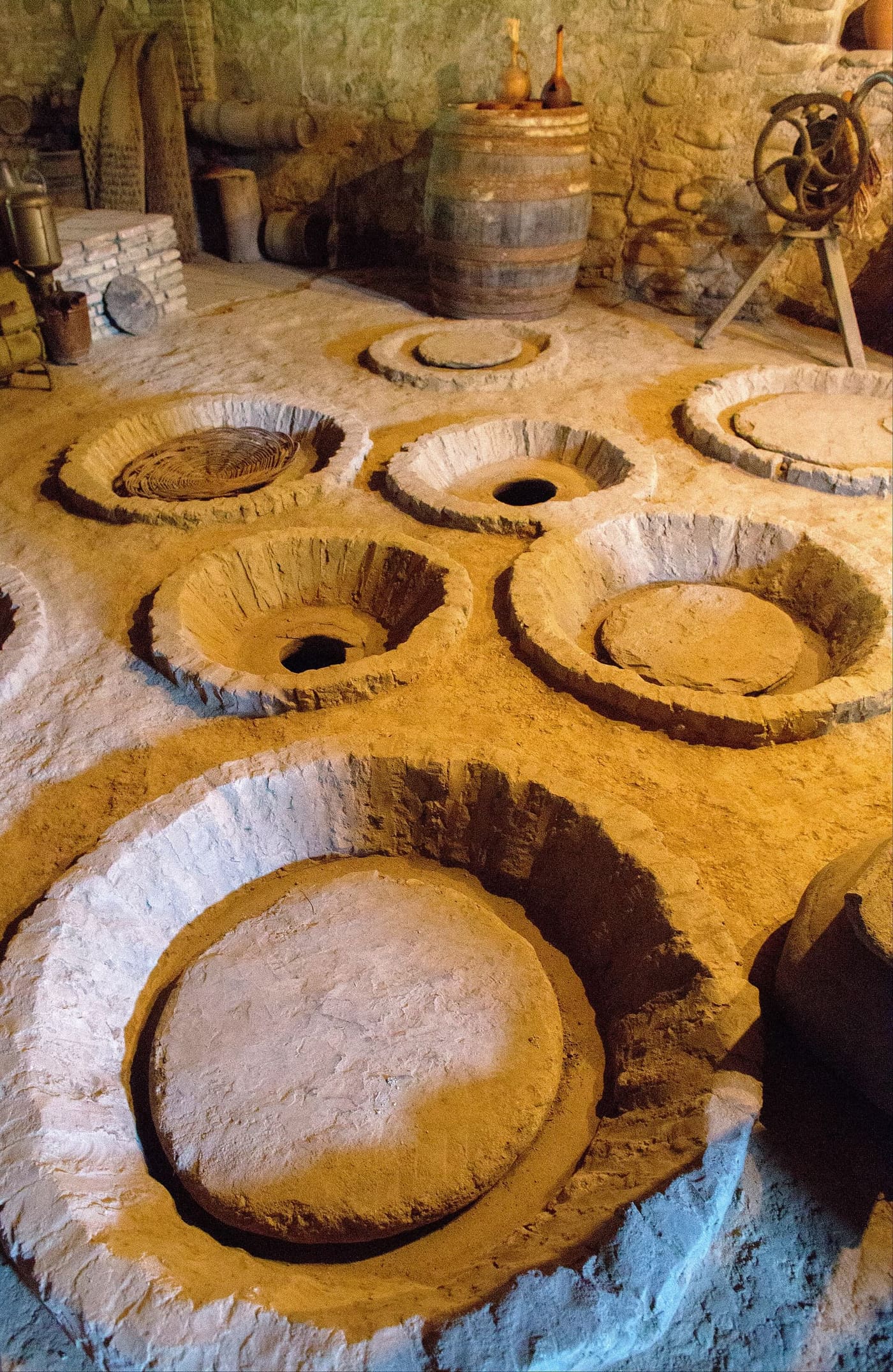 Open and sealed qvevri set into the stone floor of a traditional wine cellar in Kakheti, Georgia.