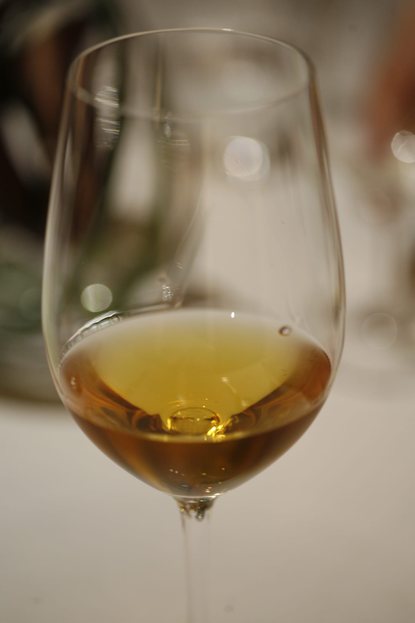 一张近距离照片，琥珀色 Tokaji 酒盛在高脚杯中，后方酒瓶与餐桌虚化。