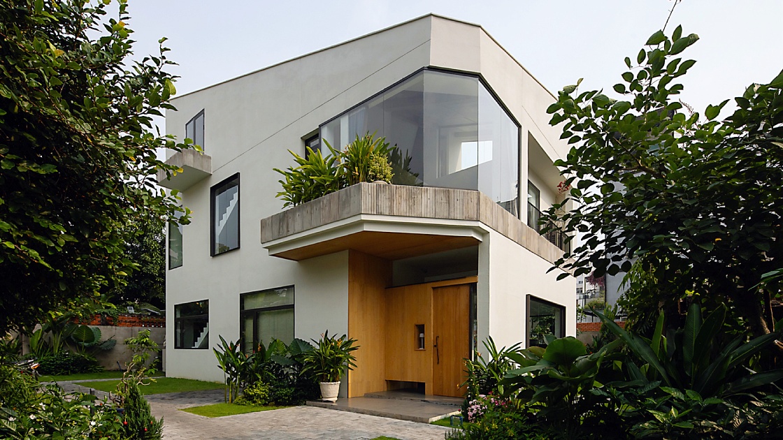 A modern white two-story villa with a wood entrance surrounded by tropical greenery, home to CieL in Ho Chi Minh City.