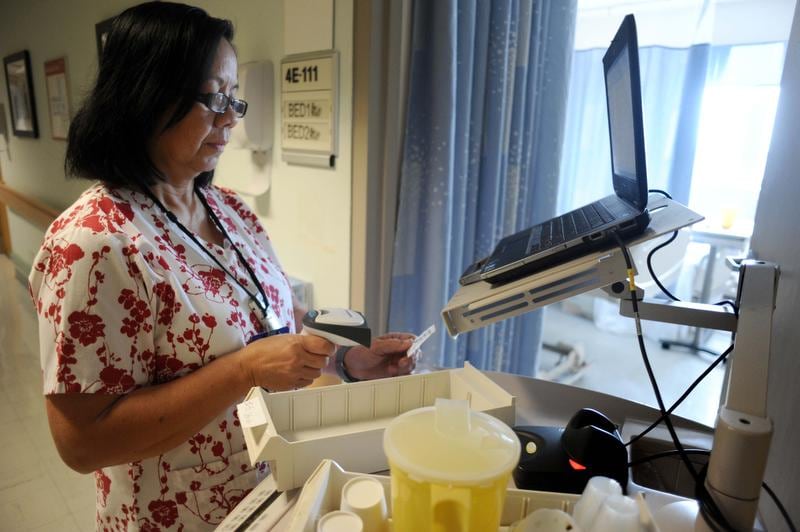 Photograph of a nurse at the Washington D.C. VA Medical Center scanning medication beside a laptop workstation and bedside medication cart.