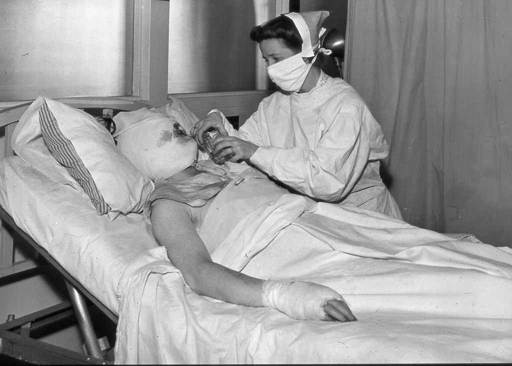 Black-and-white archival photograph of a Massachusetts General Hospital nurse caring for a bandaged survivor of the 1942 Cocoanut Grove fire.