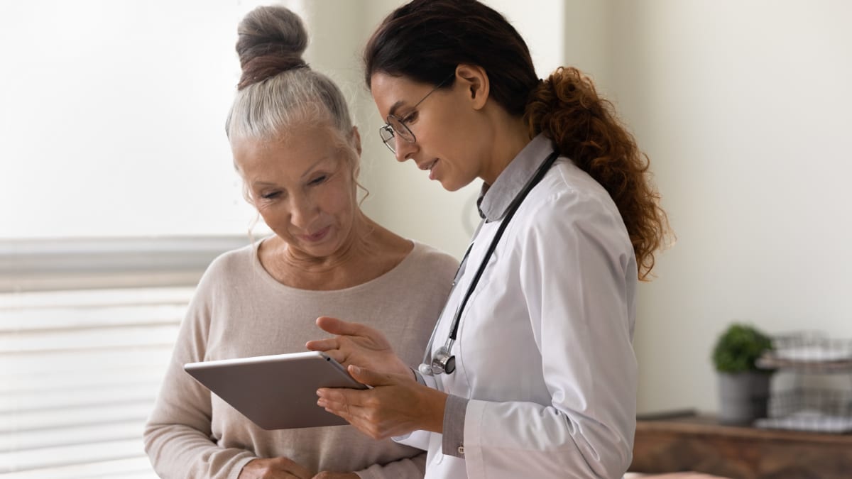Photograph of a clinician reviewing a tablet with an older patient in a clinical consultation.