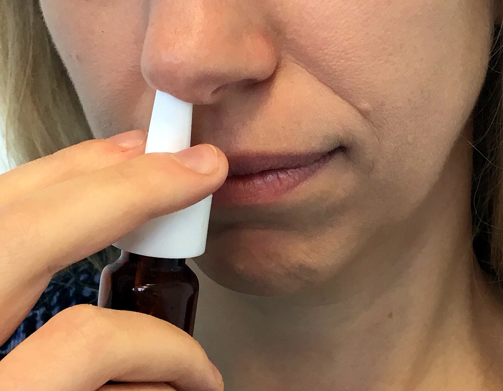 Close-up photograph of a woman holding a brown pump-spray bottle to one nostril.