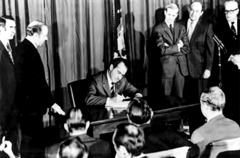 President Richard Nixon seated at a desk while officials and labor representatives crowd around him for the signing of the Occupational Safety and Health Act on December 29, 1970.