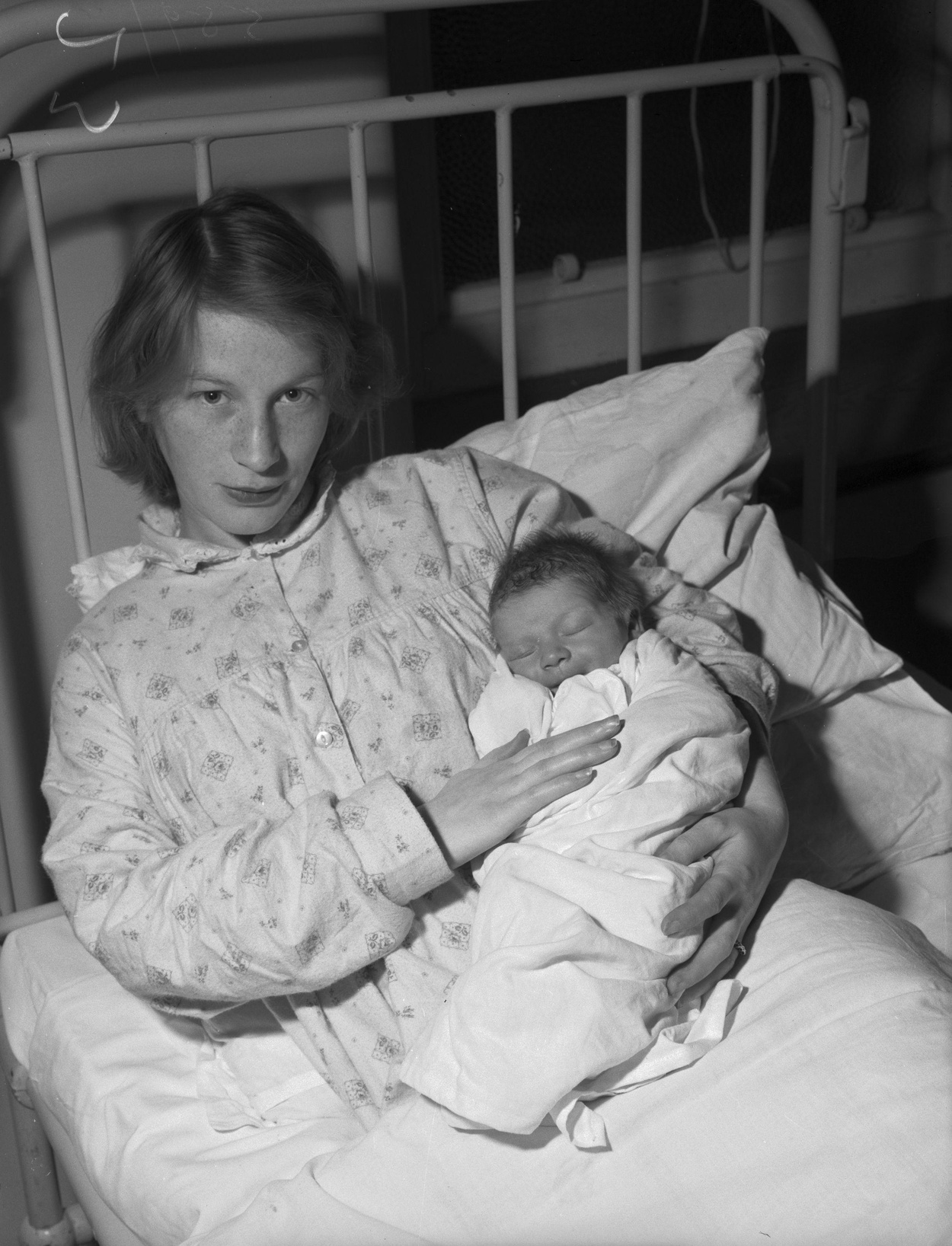 Black-and-white 1959 photograph of a mother holding her newborn in a hospital bed at Saint David's Hospital in Bangor, Wales.