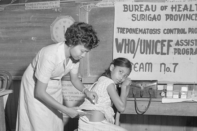 Black-and-white photograph of a health worker giving a young girl an injection beside a sign for a WHO/UNICEF-assisted treponematosis control team in Surigao Province.