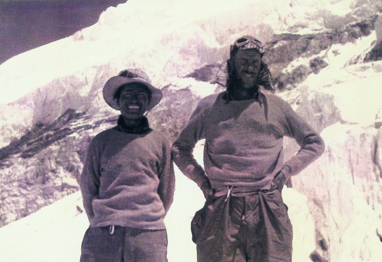 1953 年珠峰探险期间，丹增·诺盖与埃德蒙·希拉里身穿登山服，在雪地上并肩微笑。