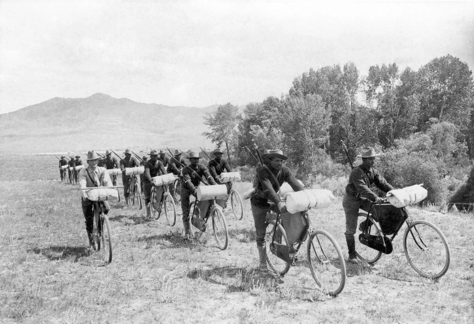 Two single-file columns of Black U.S. Army soldiers sit on heavily loaded bicycles at Fort Missoula in 1897 while Lieutenant James A. Moss rides beside them.
