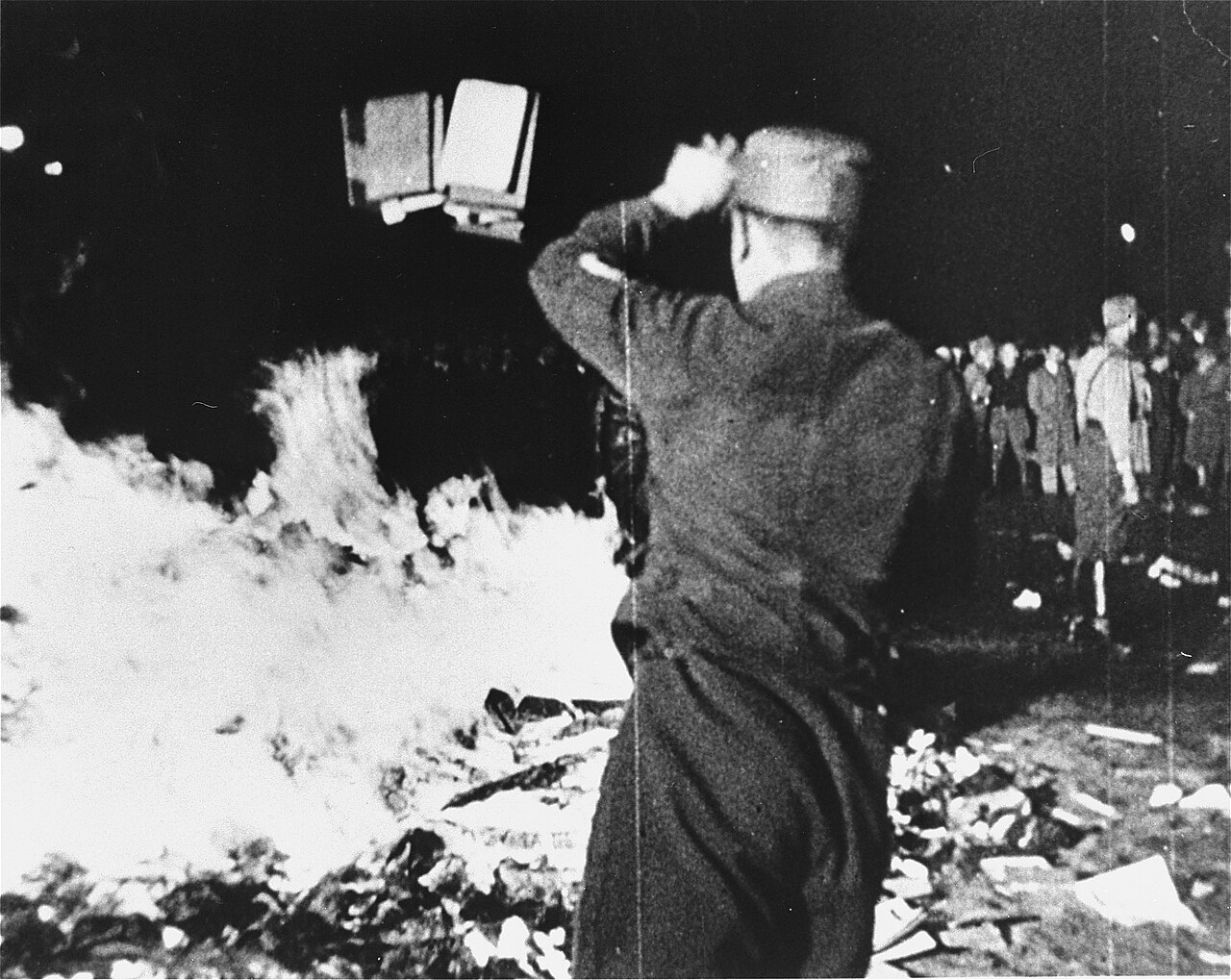 Black-and-white archival photograph of a man throwing confiscated books into a bonfire during the May 10, 1933 Nazi book burning on Berlin's Opernplatz.