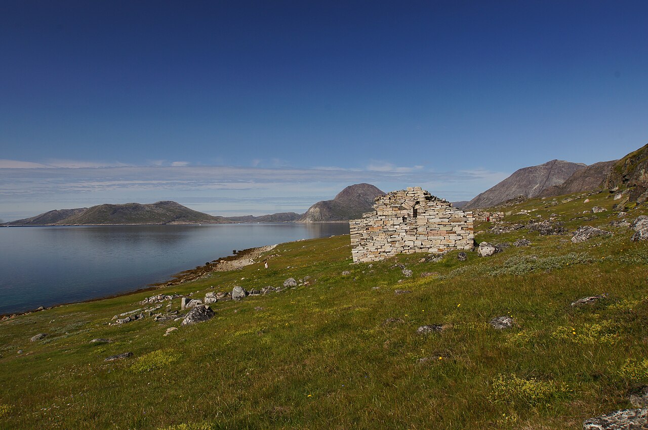 The roofless stone church at Hvalsey beside a Greenland fjord, surrounded by green pasture and rocky mountains.