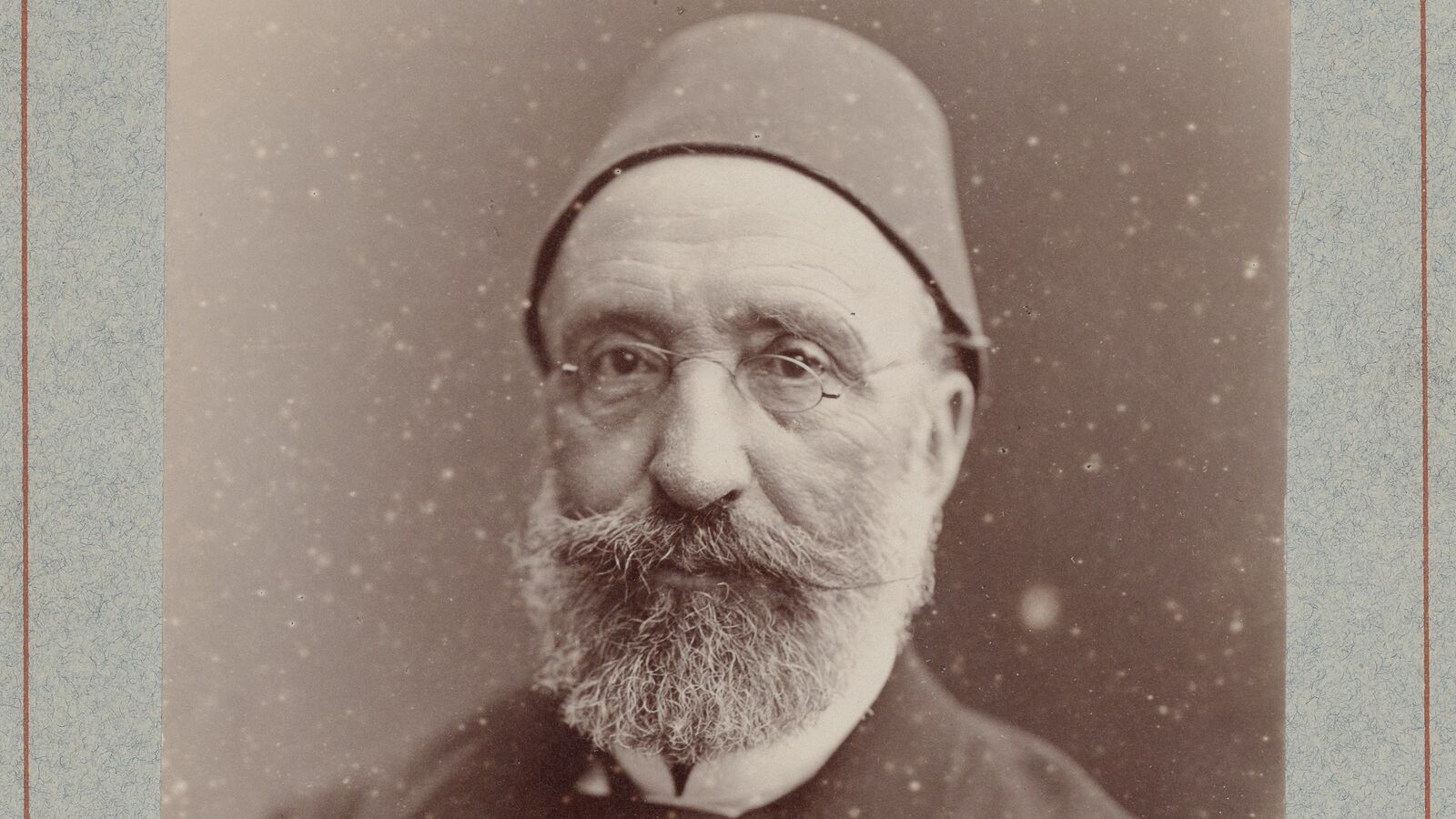 Sepia Atelier Nadar portrait of Midhat Pasha wearing a fez and pince-nez, framed by the pale blue edge of its archival mount.