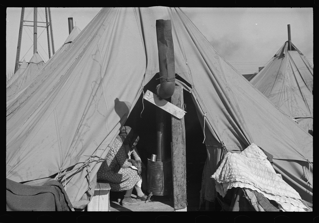 A Black woman seated at the entrance of a relief tent in a Resettlement Administration flood refugee camp in Forrest City, Arkansas, in February 1937.
