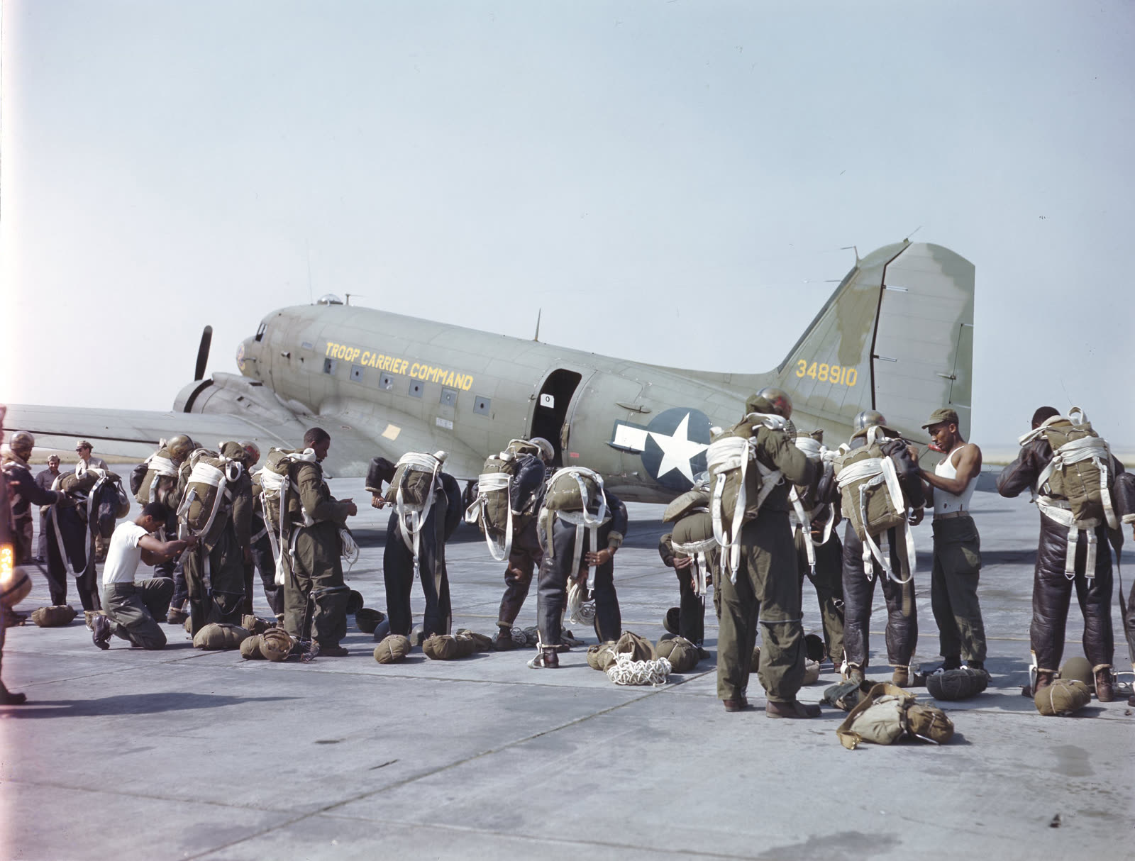 Color archival photograph of Black soldiers in the 555th Parachute Infantry Battalion fastening parachute harnesses beside a C-47 before a Project Firefly mission in Oregon in 1945.