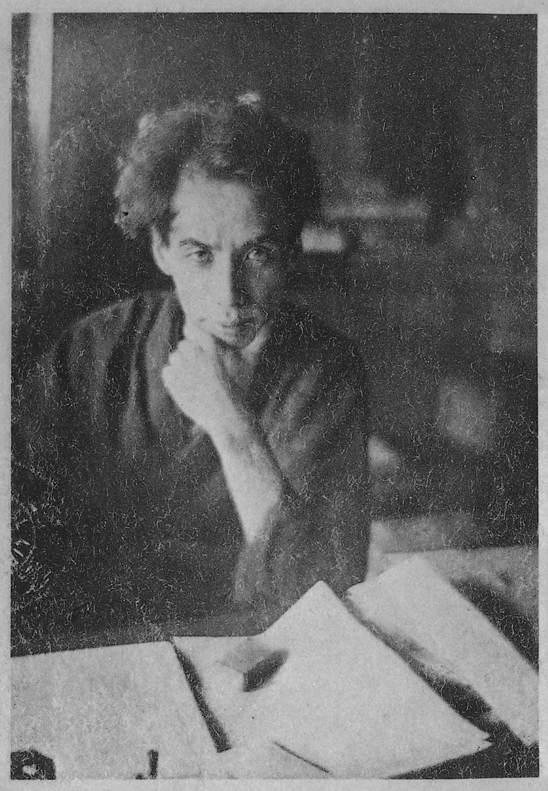Black-and-white archival portrait of Ryunosuke Akutagawa seated at a desk, resting his chin on one hand and looking toward the camera.