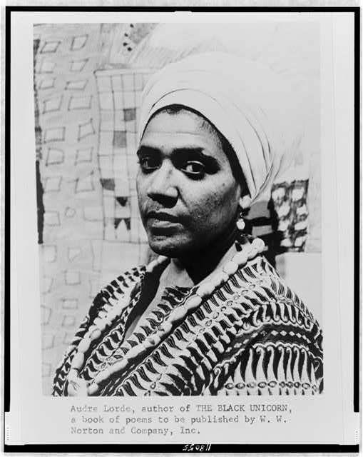 Black-and-white archival portrait photograph of Audre Lorde wearing a head wrap and patterned top, turned slightly to the side.