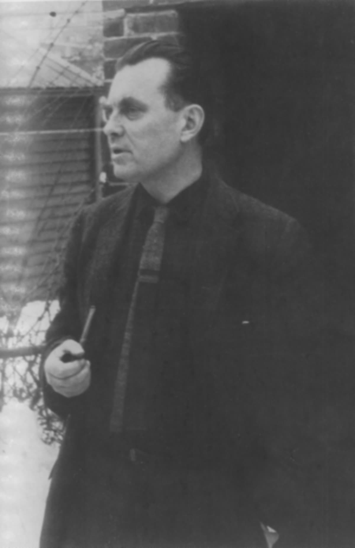 Archival black-and-white photograph of Czeslaw Milosz standing outdoors in a dark coat.