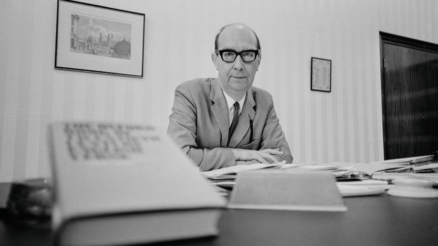 Black-and-white archival photograph of Philip Larkin seated behind a desk in his University of Hull librarian’s office.