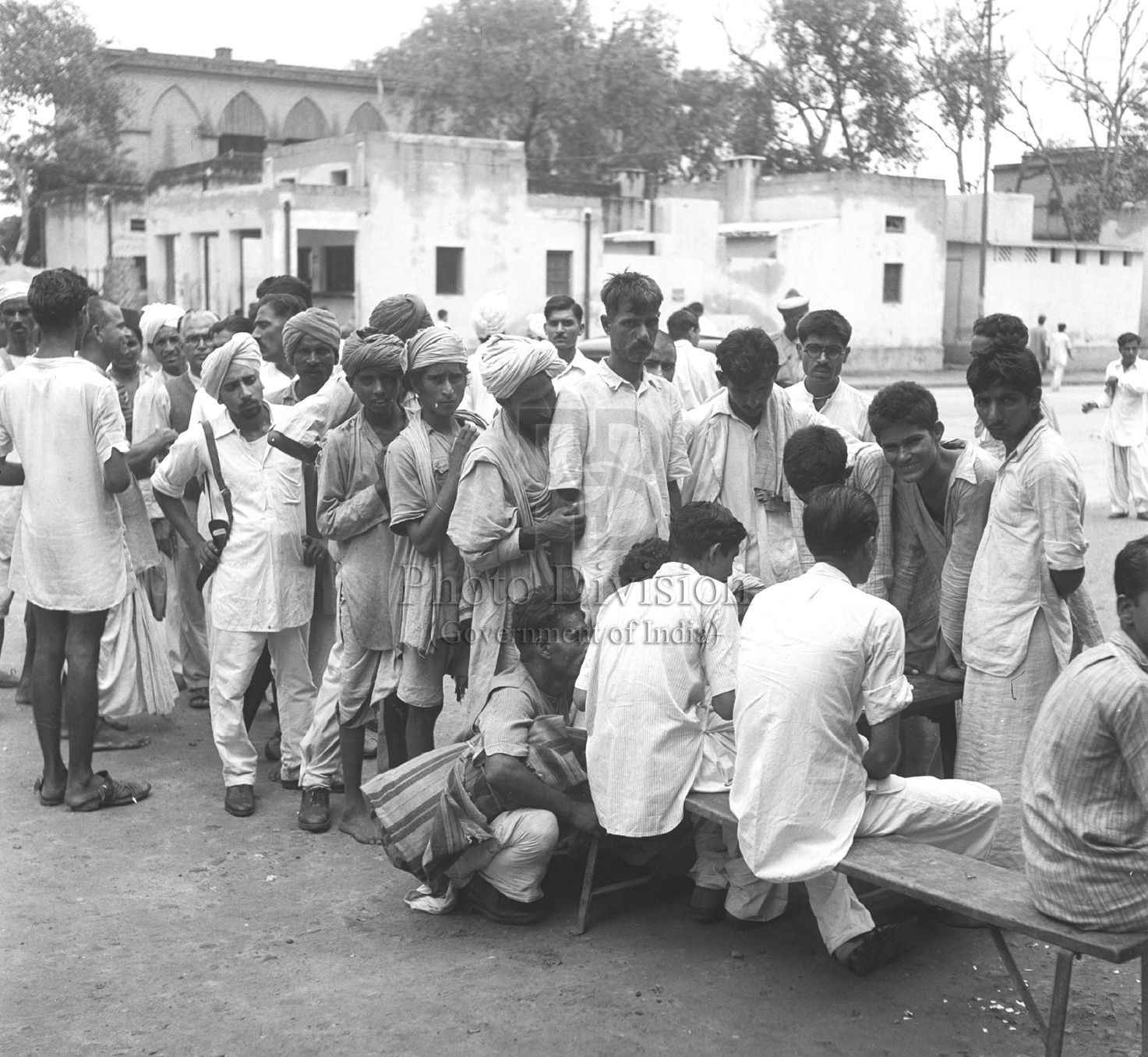 Black-and-white 1947 photograph of refugees from West Punjab gathered around a registration table before entering camps.