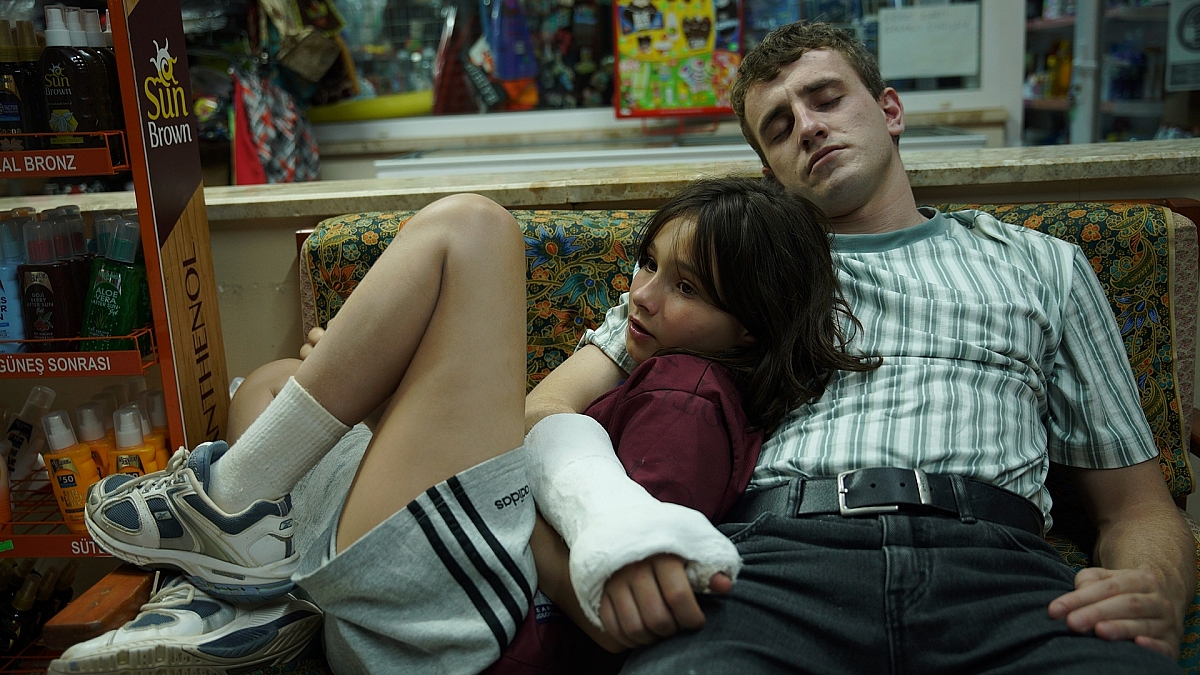Sophie rests against Calum as he sleeps in a Turkish resort shop in an official still from Aftersun.