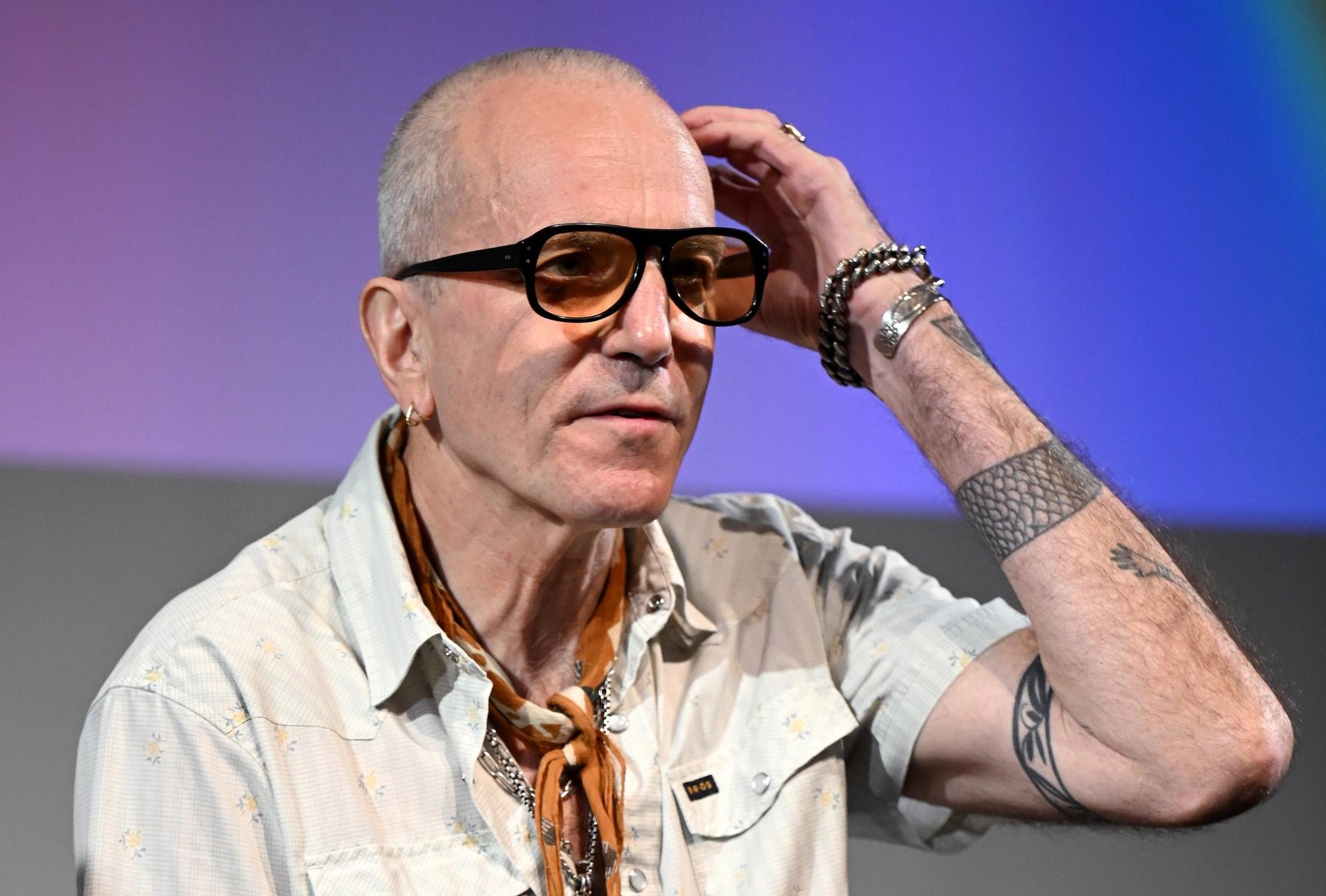Daniel Day-Lewis raises one hand to his head while speaking onstage in amber-tinted glasses at the 2025 BFI London Film Festival.
