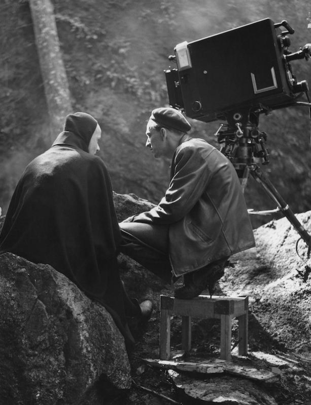 Black-and-white 1956 production photograph of Ingmar Bergman seated beside Bengt Ekerot in Death's hooded costume during The Seventh Seal.