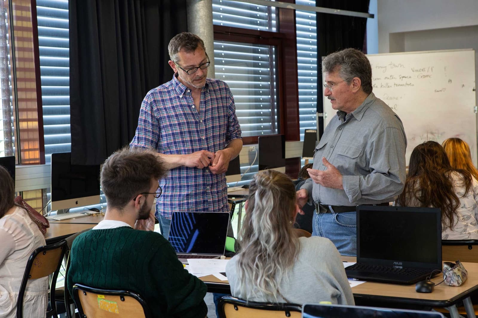 Title designer Dan Perri speaks with another man in a computer classroom as students work at tables in the foreground.