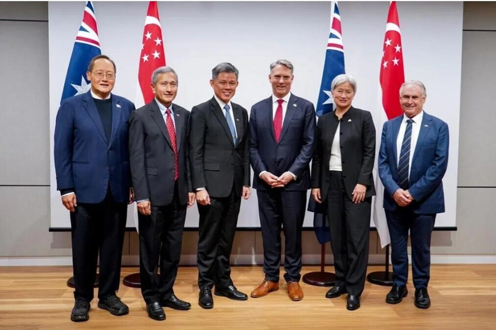 Six Singaporean and Australian ministers stand together between the two countries’ flags in Adelaide.