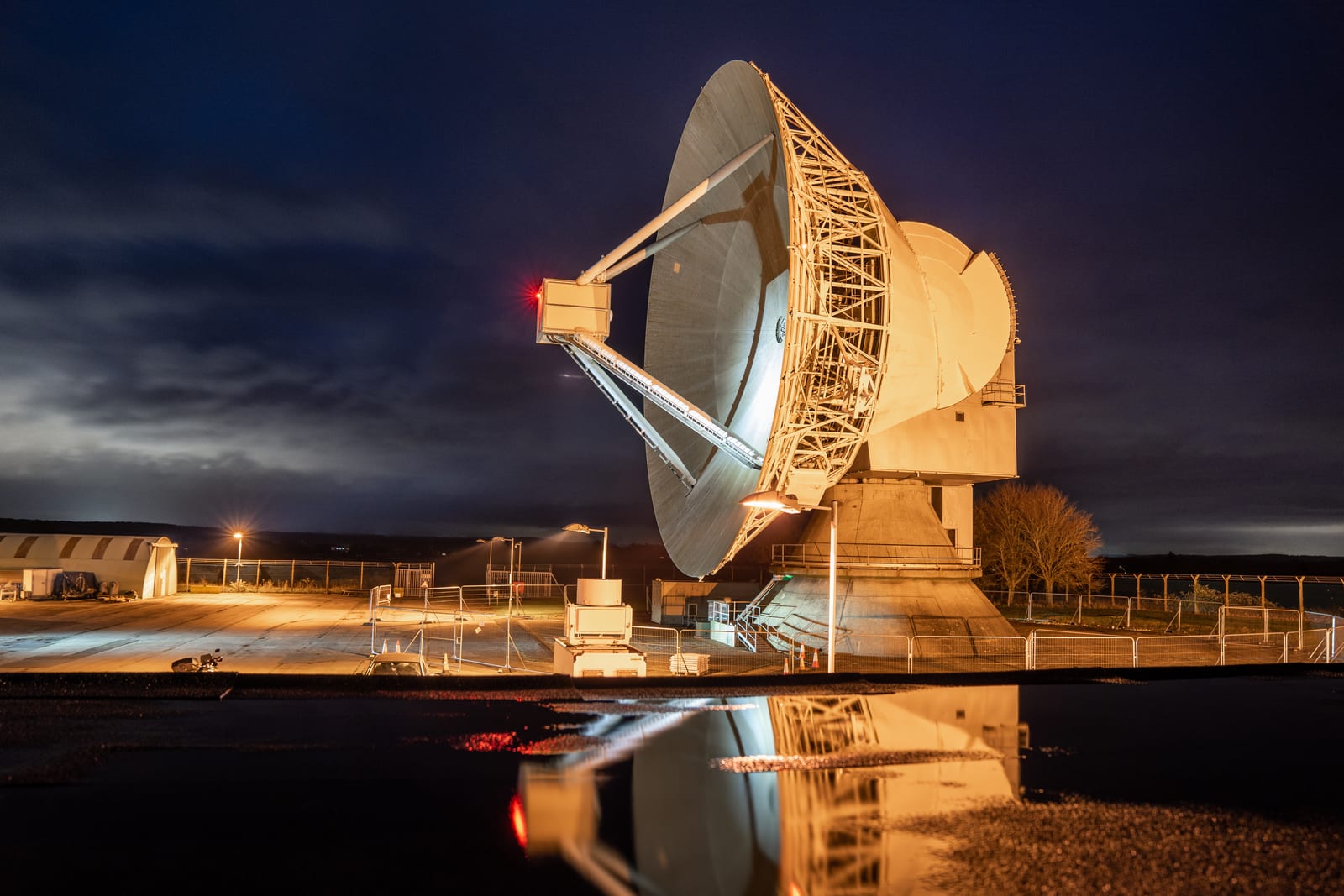 The illuminated 25-metre Chilbolton radio telescope stands beneath a dark, clouded night sky.
