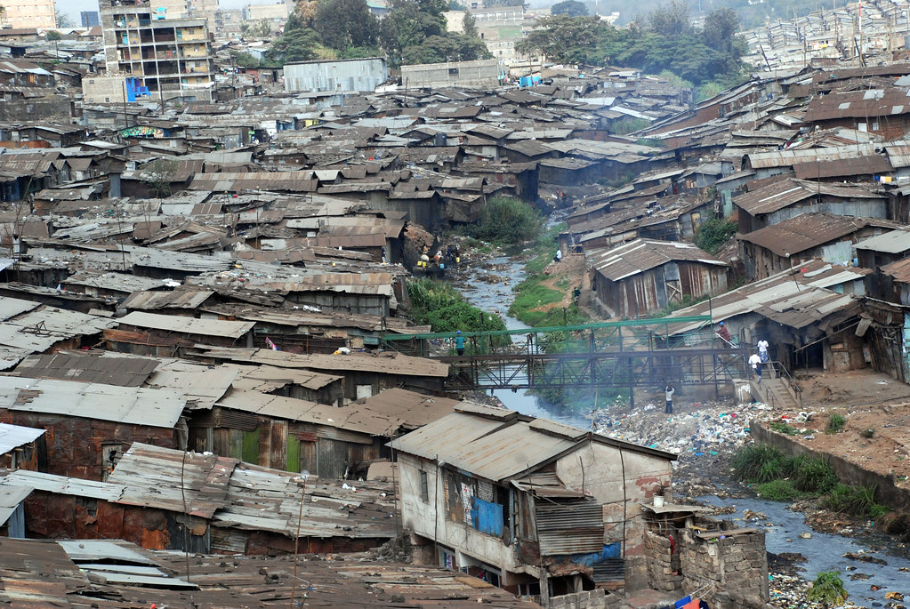 Elevated view across densely packed corrugated roofs, a stream and footbridges in Mathare, Nairobi.