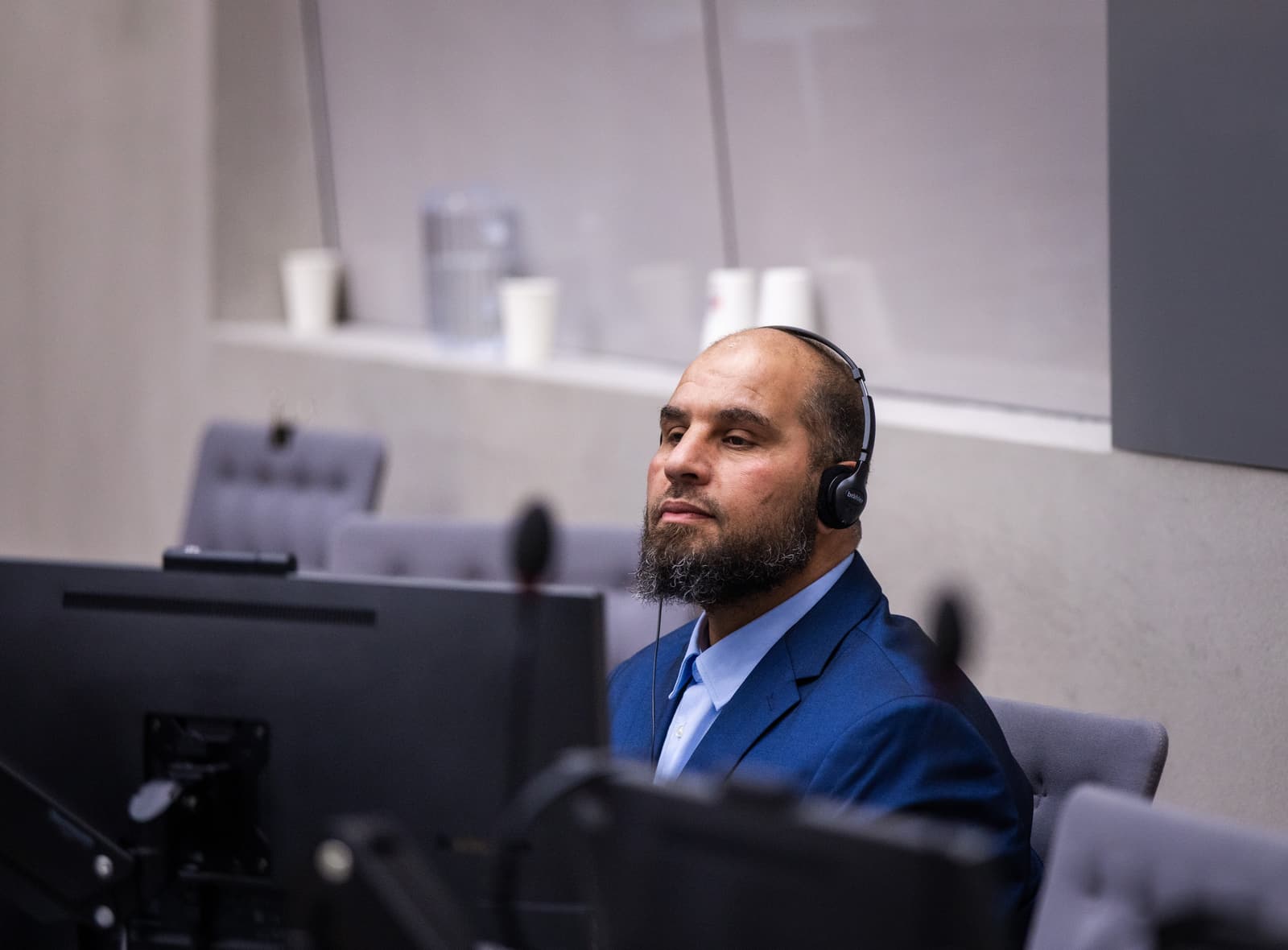 Khaled Mohamed Ali El Hishri wearing headphones and a blue suit inside an International Criminal Court courtroom.