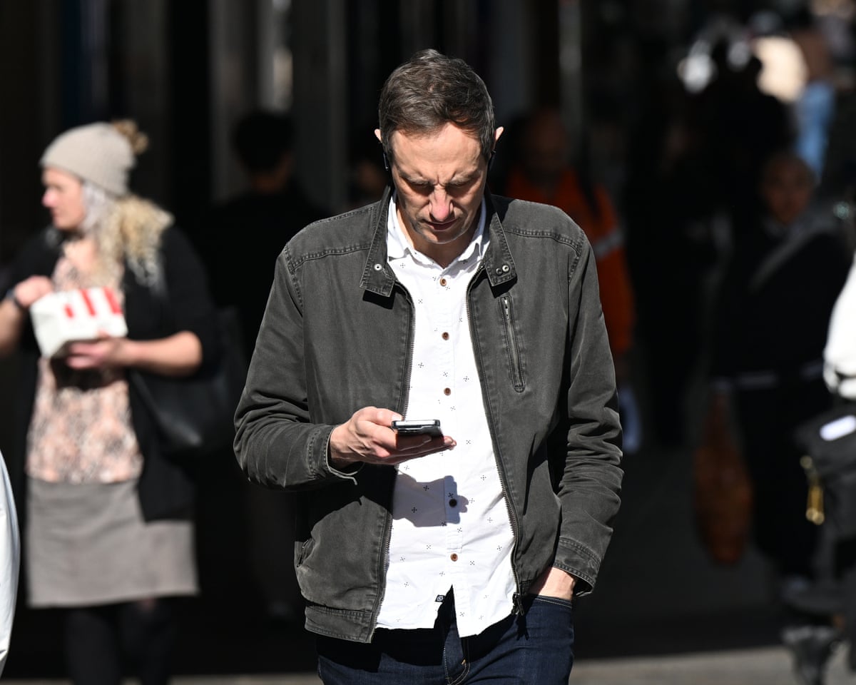 A person outdoors looks down at a mobile phone during Australia’s national AusAlert test.