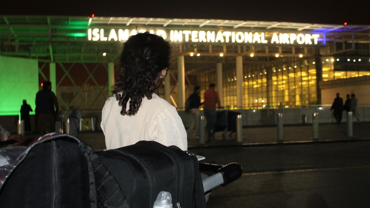 A traveler seen from behind waits beside piled luggage outside Islamabad International Airport at night.