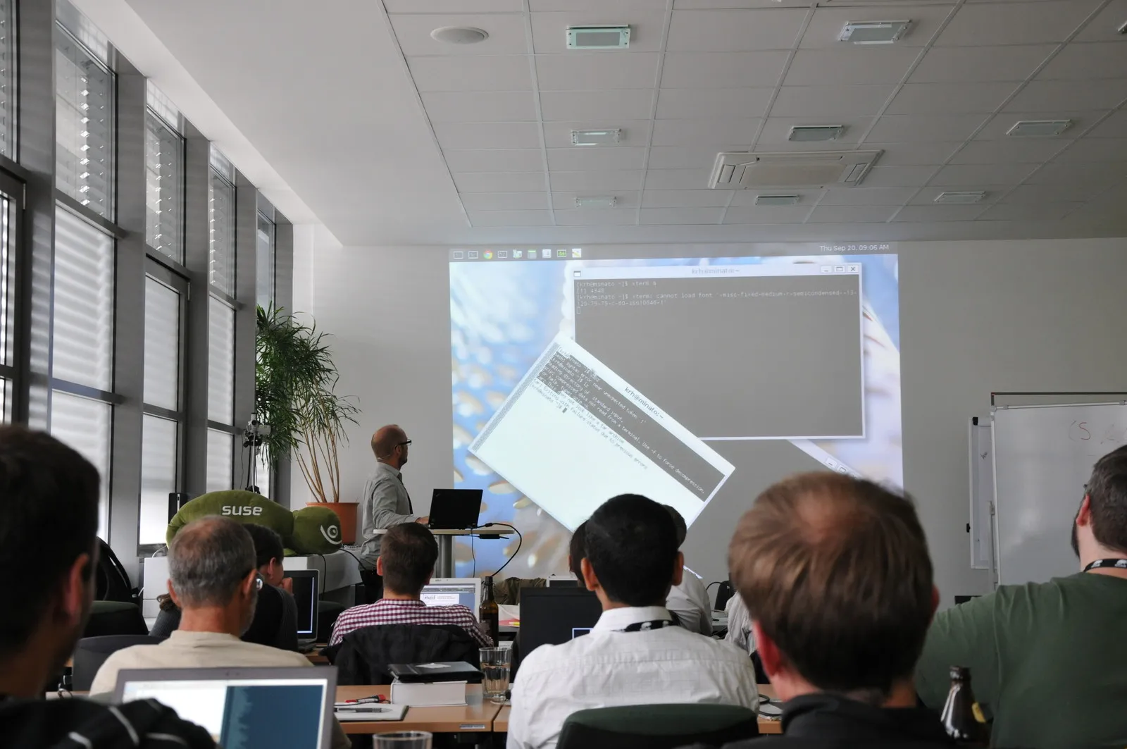 A presenter addresses attendees at an X.Org Developers Conference technical session with terminal windows projected at the front of the room.