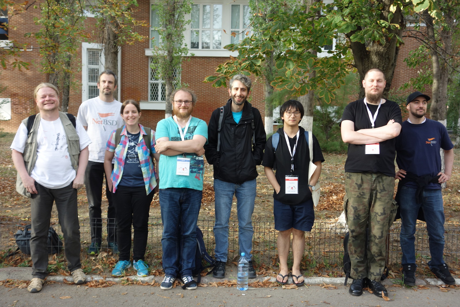 Eight NetBSD contributors wearing conference badges stand outside a brick building during a developer summit.