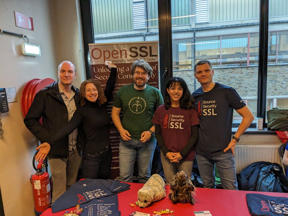 OpenSSL 贡献者和工作人员站在 FOSDEM 2024 的 OpenSSL 展台后。