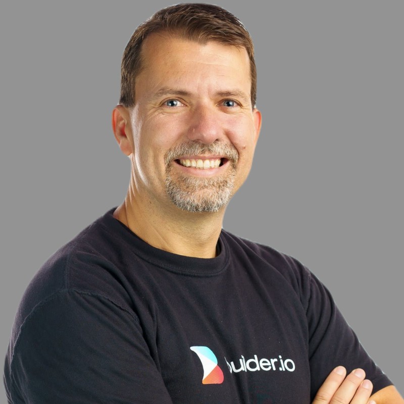Misko Hevery in a QCon speaker portrait, smiling with arms crossed against a gray background.