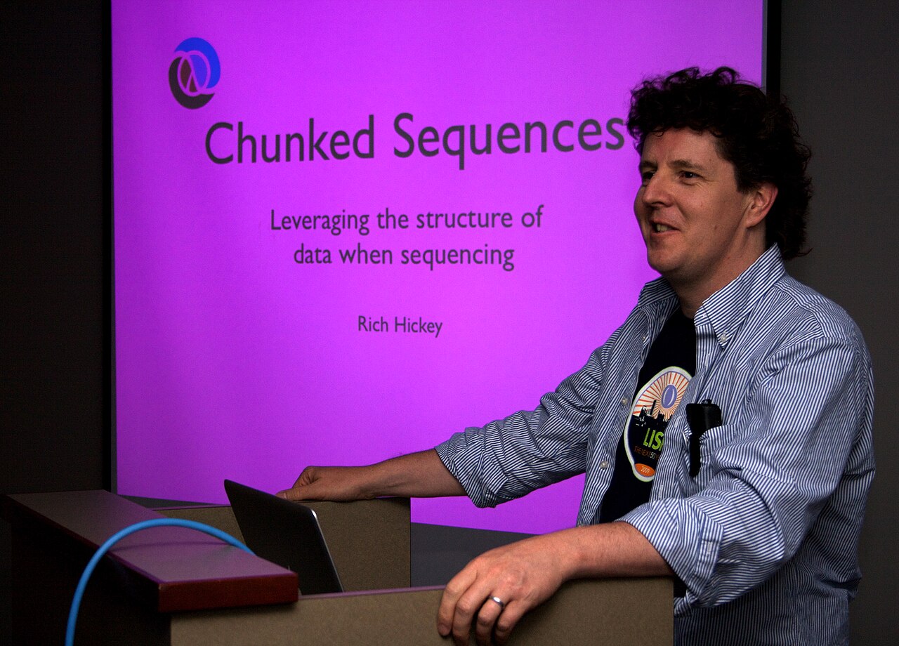 Rich Hickey standing at a lectern beside a projected slide titled Chunked Sequences at a 2009 software event.